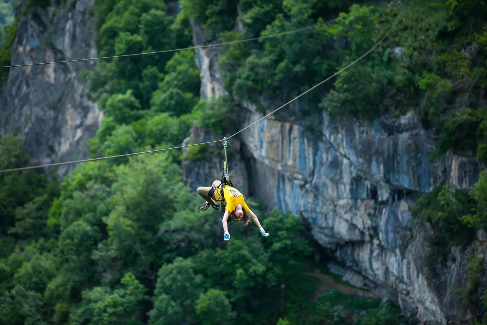 Rider in a yellow shirt on the zipline below the cliff